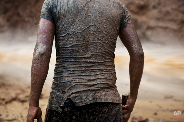 In this May 4, 2014 photo, a miner continues his search for gold in mud-drenched clothes inside a crater at an illegal gold mine process in La Pampa in Peru's Madre de Dios region. The informal miners of La Pampa know they will soon be evicted, their engines blown up and settlements burned after Peru’s government declared all informal mining illegal on April 19. The government claims that the informal miners have destroyed the surrounding forests and polluted the environment by using mercury in the gold extraction process. (AP Photo/Rodrigo Abd)