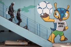 Riot police walk next to a mural of the mascot for the 2014 World Cup soccer tournament, called Fuleco, near the Maracana stadium, after evicting Indians from the nearby old Indian Museum in Rio de Janeiro, Friday, March 22, 2013. Police in riot gear invaded an old Indian museum complex Friday and pulled out a few dozen indigenous people who for months resisted eviction from the building, which will be razed as part of World Cup preparations next to the legendary Maracana football stadium. (AP Photo/Felipe Dana)
