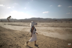 In this photo taken Friday, June 6, 2014, An Israeli woman wears a unicorn mask as she walks in the playa during Israel's first Midburn festival, modeled after the popular Burning Man festival held annually in the Black Rock Desert of Nevada, in the desert near the Israeli kibbutz of Sde Boker. Some 3,000 people set up a colorful encampment in the dusty moonscape, swinging from hoops by day and burning giant wooden sculptures by night. For five days, participants mostly Israelis created a temporary city dedicated to creativity, communal living, and what the festival calls "radical self-expression." (AP Photo/Oded Balilty)