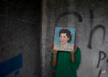 In this Wednesday, July 30, 2014 photo, a young Honduran migrant who didn't want his face to appear in photos hides behind a painting he found in a guard shack, while waiting with a group of migrants for a northbound train, in Huehuetoca, outside Mexico City. The migrant was one of three young Honduran brothers traveling north together in hopes of finding work in the U.S. Days earlier, they said, they had been robbed along with two dozen other passengers while riding a train. (AP Photo/Rebecca Blackwell)