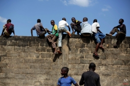 Children out of school climb a wall to see a civilian helicopter land in Gueckedou, Guinea, Friday, Nov. 21, 2014. Officials in Guinea say bandits during a roadside robbery stole a cooler containing blood samples that are believed to have Ebola, from a vehicle traveling from Kankan prefecture in central Guinea to a test site in Gueckedou, in the south. (AP Photo/Jerome Delay)