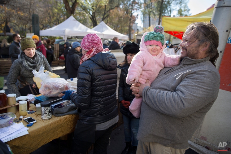 In this Saturday, Nov. 22, 2014, photo, Paul Dench-Layton, of Violet Hill Farm, holds his daughter Lillianna Grace, as customers pick up their Thanksgiving turkeys at the Union Square Farmers Market, in New York. The market, and various high-end Manhattan restaurants, are the farms' entire consumer base. (AP Photo/John Minchillo)
