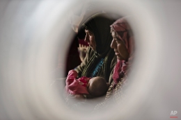 Seen through an air vent of a tent a Syrian Kurdish refugee woman from the Kobani area holds a child on a cold morning at a camp in Suruc, on the Turkey-Syria border Monday, Nov. 17, 2014. (AP Photo/Vadim Ghirda)
