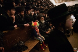 A child dressed in a clown costume, participates with other Ultra-Orthodox Jewish men in the Purim festival at a synagogue in Jerusalem, Thursday, March 8, 2012. The Jewish holiday of Purim celebrates the Jews' salvation from genocide in ancient Persia, as recounted in the Scroll of Esther. (AP Photo/Bernat Armangue)