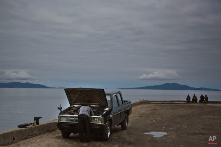 In this June 21, 2014 photo, a man works on his car as others sit next to the sea Wonsan, North Korea. (AP Photo/David Guttenfelder)