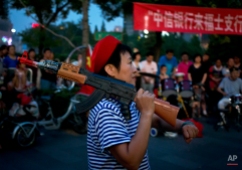 A Chinese woman holds a toy gun on her shoulder while she dances at a square outside a shopping mall in Beijing, China, Sunday, June 29, 2014. Local residents in the capital city frequently gather at public squares or parks to take part any performances their daily fitness activities. (AP Photo/Andy Wong)