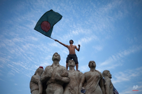 A Bangladeshi cricket fan waves the Bangladeshi flag standing atop a sculpture as hundreds gather to celebrate their team's victory in the World Cup match against England at the Dhaka University Campus in Dhaka, Bangladesh, Monday, March 9, 2015. Bangladesh defeated England by 15-runs Monday to enter the quarterfinals. (AP Photo/Suvra Kanti Das)