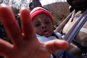 In this Saturday, Feb. 28, 2015 photo 10-months-old migrant Christian Djeukam reaches out to the lens of the photographer as he sits in a baby carrier near the town of Evzonoi, Greece.(AP Photo/Dalton Bennett)
