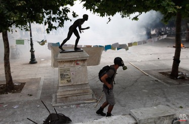 A masked protester walks in tear gas next to a statue outside of the Greek Parliament in central Athens, during a rally against plans for new austerity measures, Wednesday, June 15, 2011. (AP Photo/Lefteris Pitarakis)