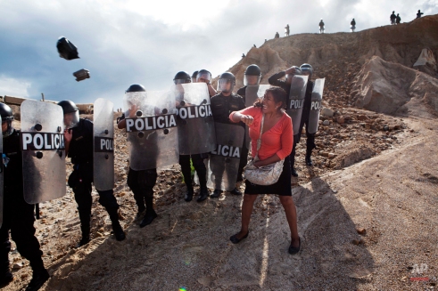 A woman throws a rock and a bag at riot policemen who block her way home in Huepetuhe district in Peru's Madre de Dios region in Peru, Monday, April 28, 2014. Soldiers, police and marines have begun destroying illegal gold mining machinery in Peru’s southeastern jungle region of Madre de Dios, enforcing a ban on illegal mining in the Huepetuhe district. Before the deadline, miners clashed with police while intermittently blocking traffic on the Interoceanic Highway that links the Pacific with Brazil. (AP Photo/Rodrigo Abd)