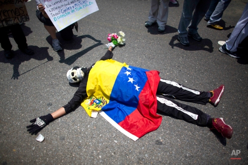 An opposition demonstrator dressed in a skeleton costume with a Venezuelan national flag draped over his body, lies on the pavement, during a May Day march in Caracas, Venezuela, Friday, May 1, 2015. Pro-government and opposition workers marched today in the midst of the political and economic crisis prevailing in the country, with separate marches that took place to mark International Workers Day also known as May Day. (AP Photo/Ariana Cubillos)