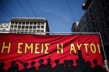 A protester holds a banner which reads: " It's either us or them", during a May Day rally in Athens, Greece, on Friday, May 1, 2015. In financially struggling Greece, an estimated 13,000 people took part in three separate May Day marches in Athens, carrying banners and shouting anti-austerity slogans. (AP Photo/Yorgos Karahalis)