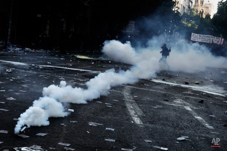 In this Oct. 20, 2011 photo, a protester throws a stone at riot police as he is seen in a smoke from a stun grenade thrown by police forces during rioting in central Athens. (AP Photo/Petros Giannakouris)