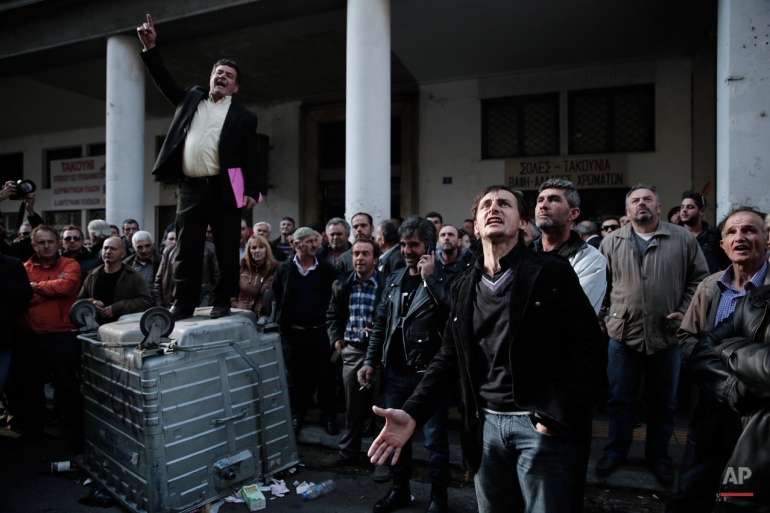 In this Tuesday, Nov. 25, 2014 photo, a farmers' union official delivers a speech on an overturned rubbish bin as protesting farmers look up at the Agriculture Ministry building during an anti bailout protest, in Athens. (AP Photo/Petros Giannakouris)