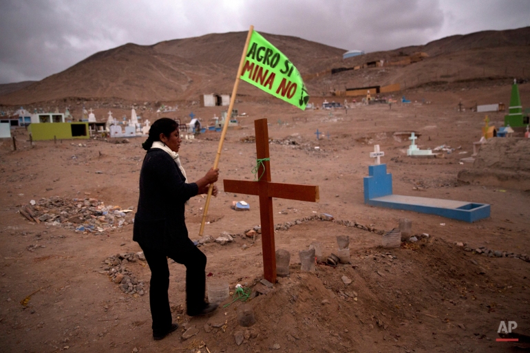 In this May 30, 2015 photo, Aracely Huayna, 36, works to place a flag with a message that reads in Spanish: "Agriculture Yes, Mining No" on a cross that adorns her father's grave, in Tambo Valley, Arequipa, Peru. Huayna says her 61-year-old father died when he was hit by a stray bullet, during recent violent protests against mining in the area. She believes riot police are responsible for his death. (AP Photo/Rodrigo Abd)