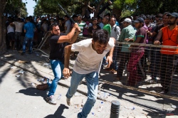 A Greek plain clothed policeman chases away Pakistani migrants as they started shouting while waiting to be registered near a police station at the southeastern island of Kos, Greece, Wednesday, Aug. 19, 2015. More than 130,000 migrants have reached Greece so far in 2015, straining the country's resources. (AP Photo/Alexander Zemlianichenko)