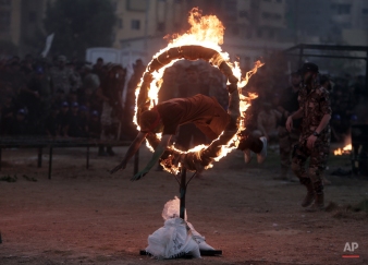 A young Palestinian jumps through a fire ring as part of a graduation ceremony of the Hamas, Liberation Youth, military summer camp, in Gaza City, Wednesday, Aug. 5, 2015. (AP Photo/ Khalil Hamra)