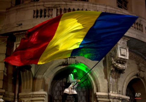 A man's face is illuminated by a laser torch as he waves a large Romanian flag, after climbing the University building, during the third day of protests, joined by tens of thousands across the country, calling for early elections, in Bucharest, Romania, Thursday, Nov. 5, 2015. Romania's President Klaus Iohannis has named the Education Minister Sorin Campeanu as interim premier following the resignation of the Prime Minister Victor Ponta and his cabinet. (AP Photo/Vadim Ghirda)