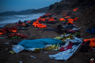 The body of a young man covered with a blue blanket remains on Eftalou beach after his dinghy capsized on the northeastern Greek island of Lesbos, Friday, Oct. 30, 2015. (AP Photo/Santi Palacios)