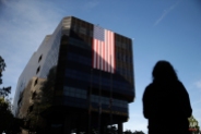 Emily Petrus, a worker for San Bernardino County, pauses to look at a large flag hanging on San Bernardino City Hall on Monday, Dec. 7, 2015 in San Bernardino, Calif. County employee's returned to work today after Wednesday's mass shooting. Thousands of employees of San Bernardino County are preparing to return to work Monday, five days after a county restaurant inspector and his wife opened fire on a gathering of his co-workers, killing 14 people and wounding 21. (AP Photo/Jae C. Hong)
