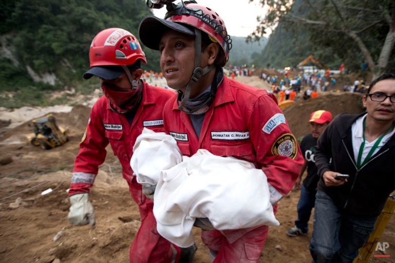 A fireman carries the body of a child recovered from the site of a landslide in Cambray, a neighborhood in the suburb of Santa Catarina Pinula, about 10 miles east of Guatemala City, Friday, Oct. 2, 2015. The hill that towers over Cambray collapsed after heavy rains, burying several houses with dirt, mud and rocks. (AP Photo/Moises Castillo)