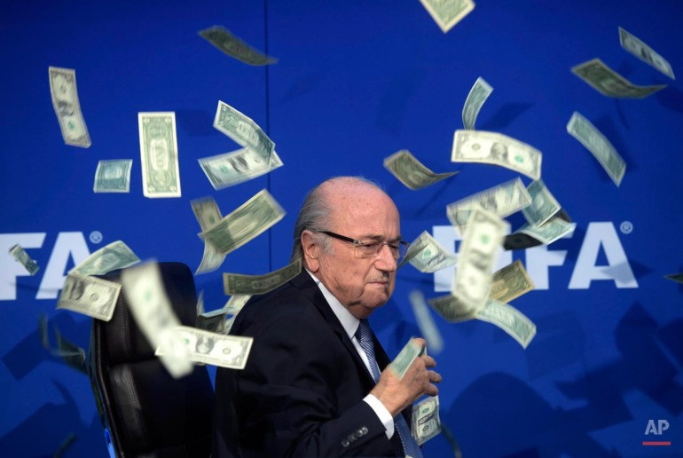 FIFA president Sepp Blatter is surrounded by banknotes thrown by British comedian Simon Brodkin during a press conference following the Extraordinary FIFA Executive Committee meeting at the headquarters in Zurich, Switzerland, Monday, July 20, 2015. Blatter and FIFA have been engulfed in a deepening corruption scandal as the sport faces criminal investigations in Switzerland and the US. (Ennio Leanza/Keystone via AP)