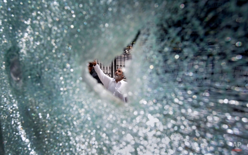 A Pakistani man, seen through shattered glass, looks at damages of a bus station after a march of supporters of a religious group towards the Parliament building turned violent in Islamabad, Pakistan, Monday, March 28, 2016. Thousands of demonstrators marched into the Pakistani capital to protest against the hanging of policeman Mumtaz Qadri in February. As the protesters reached an avenue leading to the Parliament, the march turned violent, with Qadri's supporters smashing windows and damaging bus stations. Police fired tear gas but could not subdue the crowds Sunday. (AP Photo/Anjum Naveed)