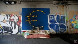 The bed of an homeless person is placed next to a mural painting of the Euro symbol, in Milan, Thursday, March 10, 2016. European Central Bank launched an unexpectedly broad array of stimulus measures Thursday aimed at boosting a modest economic recovery in the 19 countries that use the euro and nudging up dangerously low inflation. (AP Photo/Luca Bruno)
