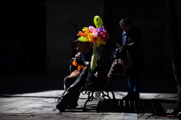 A man sits in a street bench as he shapes balloons into animals and flowers in Madrid, Spain, Friday, March 11, 2016. (AP Photo/Francisco Seco)