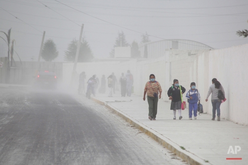 People walk on the ash-covered streets of San Andres Cholla, Mexico, Monday April 18, 2016, after the Popocatepetl volcano erupted overnight, spewing ash on nearby towns. Officials there are urging to people to wear masks to avoid inhaling the fine grit that has covered houses and cars. (AP Photo/Pablo Spencer)
