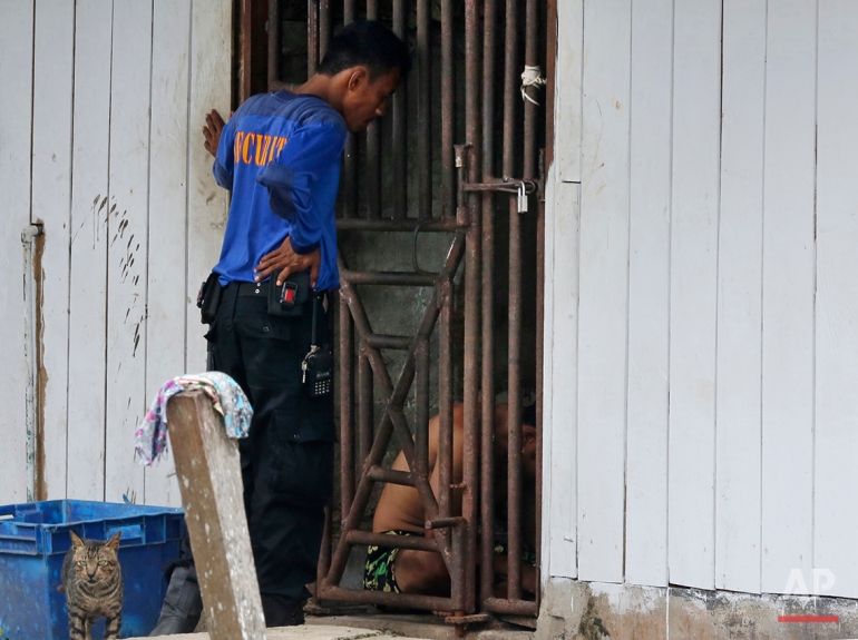 In this Nov. 2014, photo, a security guard talks to detainees inside a cell at the compound of a fishing company in Benjina, Indonesia. The imprisoned men were considered slaves who might run away. They said they lived on a few bites of rice and curry a day in a space barely big enough to lie down, stuck until the next trawler forces them back to sea. In its first report on trafficking around the world, the U.S. criticized Thailand as a hub for labor abuse. Yet 14 years later, seafood caught by slaves on Thai boats is still slipping into the supply chains of major American stores and supermarkets. (AP Photo/Dita Alangkara)
