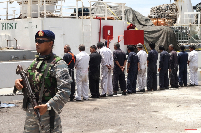 Navy personnel stand guard as the crew of Silver Sea 2, a Thai-owned cargo ship which was seized by Indonesian authorities last August, are lined up during a media conference at the port of Sabang, Aceh province, Indonesia, Friday, Sept. 25, 2015. The Thai captain of the ship has been arrested in Indonesia following allegations of illegal fishing, an official said Friday. It is the latest development linked to an Associated Press investigation that uncovered a slave island earlier this year. (AP Photo/Heri Juanda)