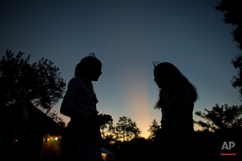 In this June 23, 2016 photo, girls talk at sunrise after an all night religious service of the church of the doctrine of the Holy Daime in Ceu do Mapia, Amazonas state, Brazil. For the service women wear shiny white crowns on their heads, green sashes over their shoulders and green belts around their waist. (AP Photo/Eraldo Peres)